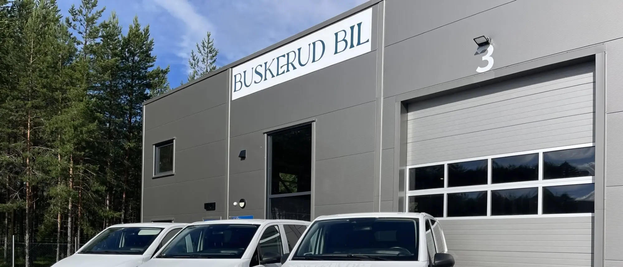 Lokalet til Buskerud Bil på Hensmoveien 10 i Hønefoss, med skiltet over inngangen og hvite varebiler parkert utenfor